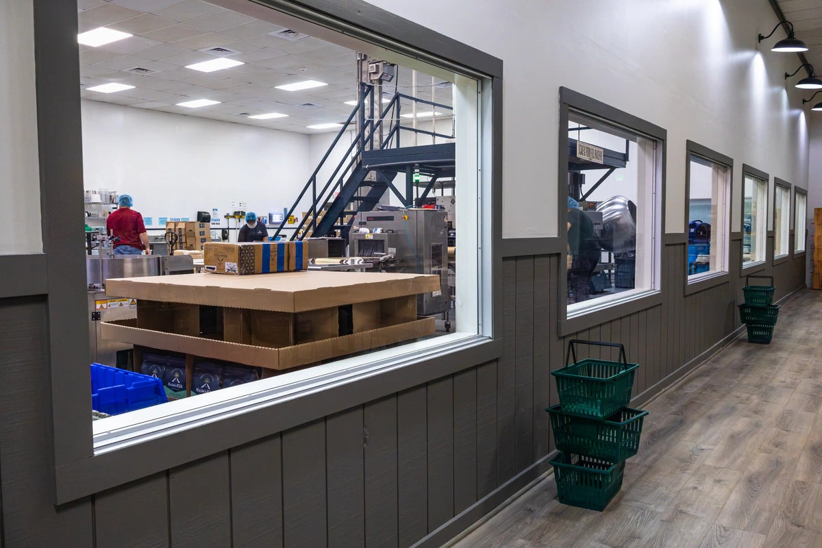 A long room with gray paneled walls and large windows looking into the cannery, where workers are visible in the background.